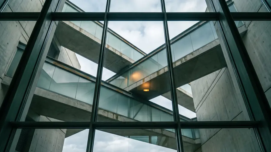 A glazed corridor of a modern building, seen from below, all green glass and steel
